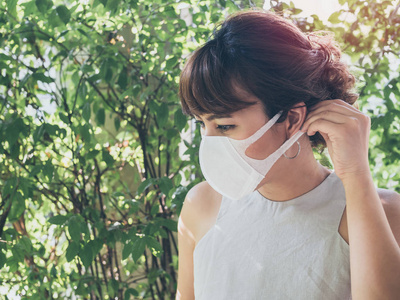 美丽的亚洲妇女戴白色防护N95防尘口罩在绿叶背景与复制空间。 防止污染的概念。