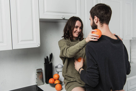 美丽的年轻幸福夫妇在厨房里橘子和互相看着