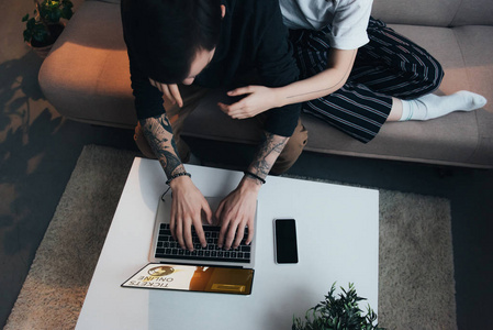 情侣坐着拥抱，一边使用笔记本电脑，一边在家中的屏幕上上网