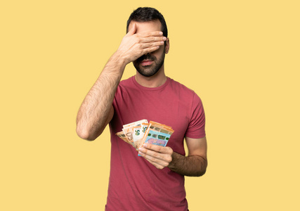 男人拿了很多钱用手遮住眼睛. 不想在孤立的黄色背景上看到什么照片