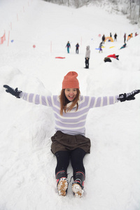 幸福微笑的年轻女人，戴着白色的帽子和温暖的外套躺在雪地上。 冬天的背景