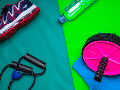 健身理念红色运动鞋瓶水和T恤滚轮绿色垫子背景顶部视图。 动机概念