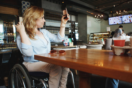 坐轮椅的女人在咖啡馆里喝咖啡，在智能手机上自拍