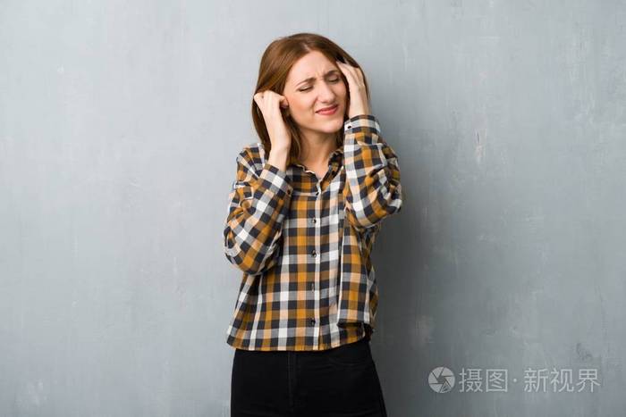 年轻的红头发女孩在肮脏的墙壁上用手捂住耳朵. 沮丧的表情