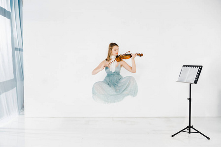 穿着蓝色连衣裙的飘浮女孩拉小提琴，背景白色的音乐支架