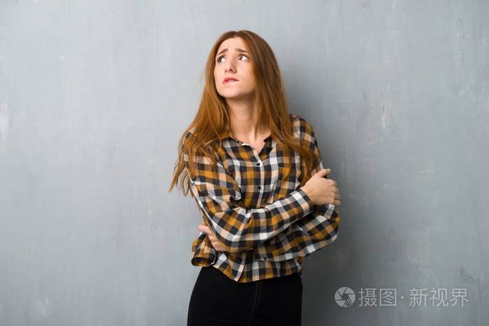 年轻的红发女孩在肮脏的墙壁上迷惑着脸的表情咬着嘴唇