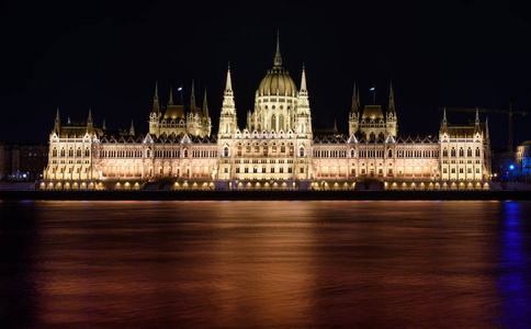 匈牙利议会大厦在布达佩斯晚上。 建筑物被点亮，多瑙河在它前面平稳地流动。