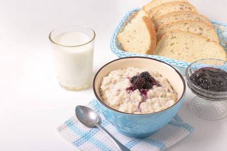 健康的早餐，有一杯牛奶，自制的燕麦片，蓝碗里的黑莓和新鲜的谷类食品面包，清淡的背景下。