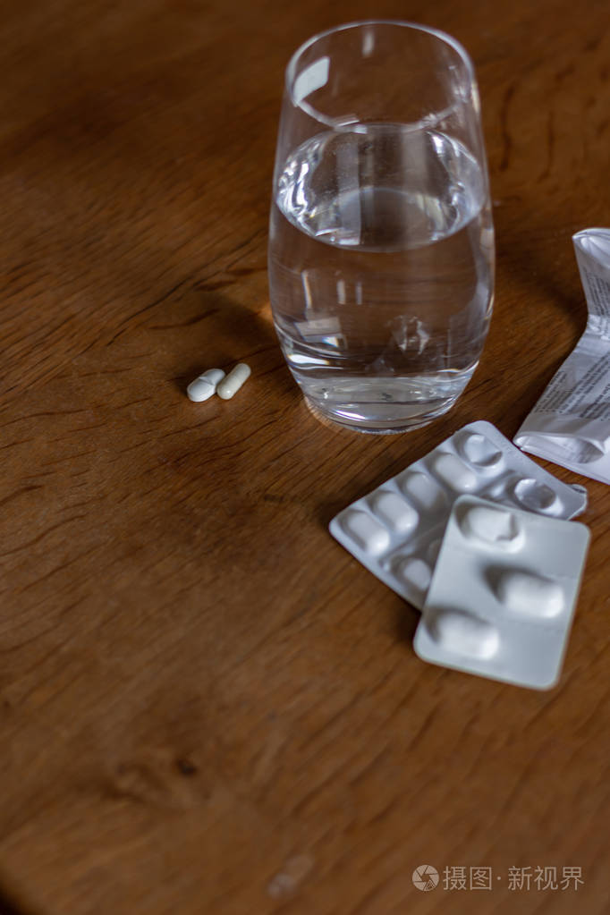 在上面的木桌上放一杯水旁边放一些药片水泡和说明书