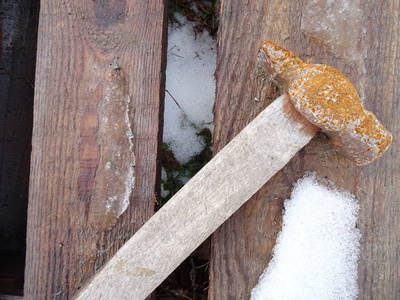 一把生锈的锤子放在覆盖着雪的老式木制背景上
