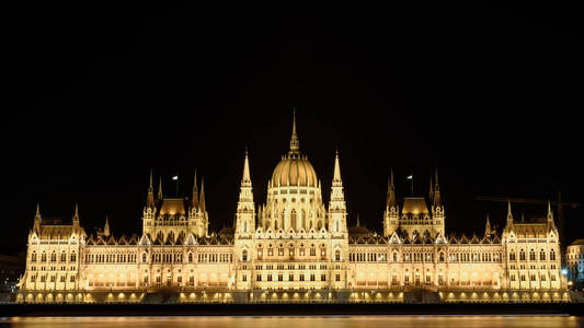 匈牙利议会大厦在布达佩斯晚上。 建筑物被点亮，多瑙河在它前面平稳地流动。