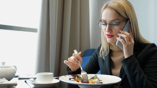 年轻的金发女经理在咖啡馆里打电话吃饭