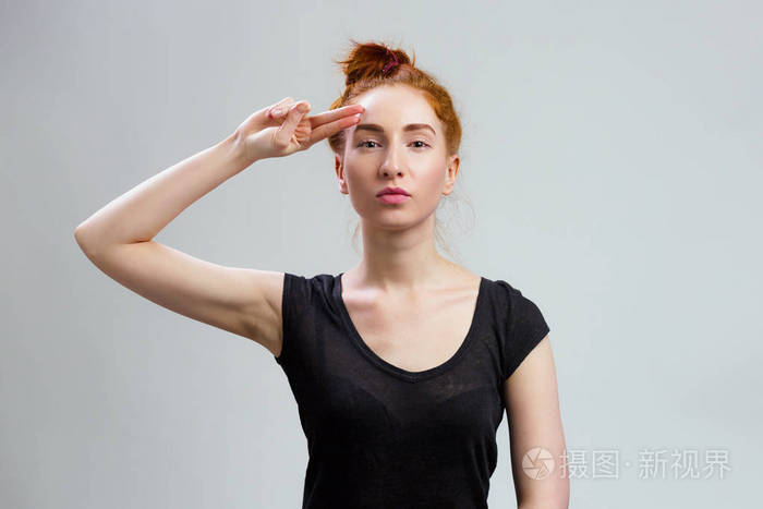 敬礼的概念年轻的红发女孩穿着休闲黑色衬衫在灰色背景的复印空间上用