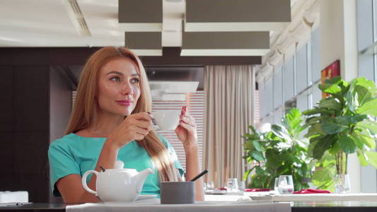华丽快乐的女人倒茶在她的杯子, 享受早餐在餐厅