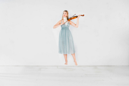 蓝色裙子的飘浮女孩在白色背景上拉小提琴，带有复制空间