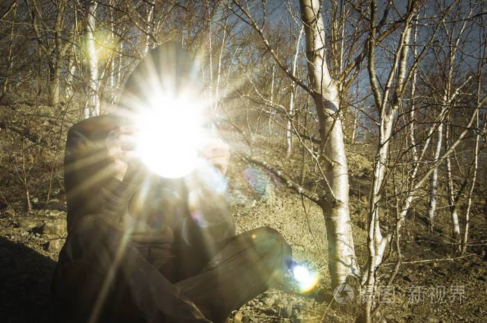 一个头戴头套的身影拿着一面反射太阳的镜子, 带着太阳耀斑