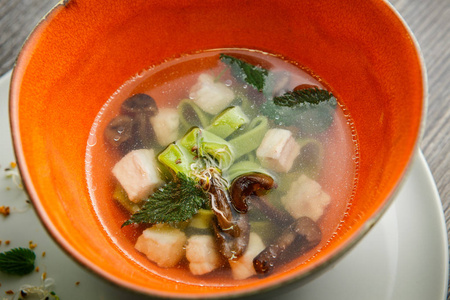 用蘑菇肉和荨麻叶在木桌上的深餐厅碗里端上美味的面条汤