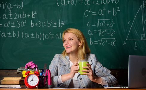 女人在教室里喝咖啡。老师与闹钟在黑板上。时间。回学校去教师节。学习和教育。现代学校。知识日。学校。家庭教育。快乐的女人