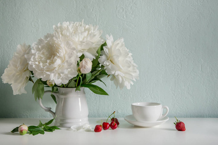 白色的花,牡丹在陶瓷花瓶里,茶和浆果在桌子上. 春天早晨的浪漫心情.