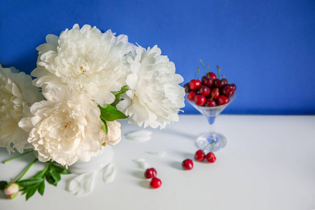 一束牡丹放在陶瓷花瓶里，茶和浆果放在桌子上，蓝色的背景上。 春天早晨的浪漫心情。