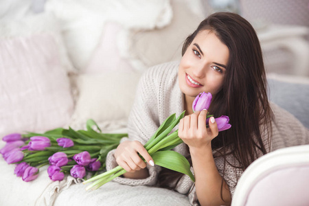 年轻迷人的女人拿着花。 一位美丽的女士，床上躺着郁金香