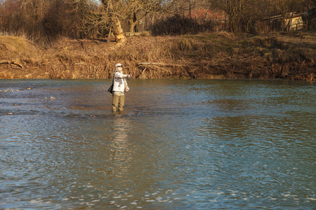 在一个晴朗的春日里，一个年轻漂亮的女人站在河里钓鱼。