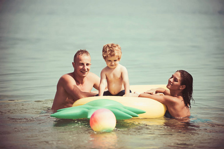 暑假和去海边旅行。菠萝充气或气垫。马尔代夫或迈阿密海滩活动的喜悦。父亲和母亲带着儿子在水里玩球。加勒比海快乐家庭情侣