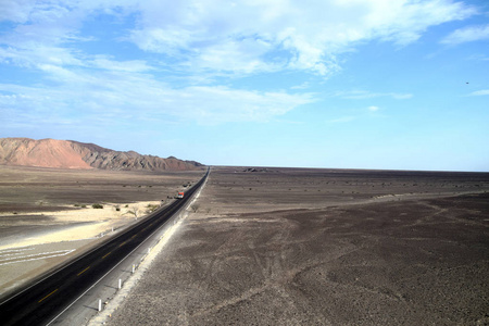 穿过沙漠的道路，远处的道路上只有一辆孤独的卡车。 背景中的蓝天和山脉。 就在纳斯卡秘鲁郊外拍摄的照片
