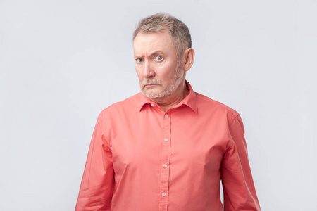 身穿红色衬衫的老人皱着眉头斜视, 表现出不相信或怀疑