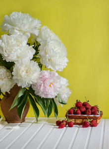 一大束牡丹放在粘土花瓶里，一碗草莓放在树桌上。 浪漫的心情。