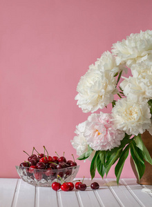 一大束牡丹放在陶瓷花瓶里，放在桌子上，樱桃放在碗里。 浪漫的心情。