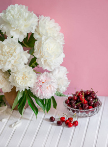 一大束牡丹放在陶瓷花瓶里，放在桌子上，樱桃放在碗里。 浪漫的心情。