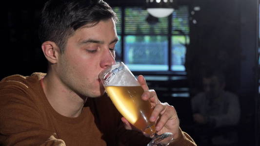 迷人的男人从他的杯子里喝着美味的啤酒, 在酒吧放松一下