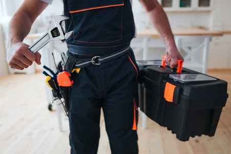 切去杂工拿着工具箱的视线, 手里拿着扳手.他站在厨房里.