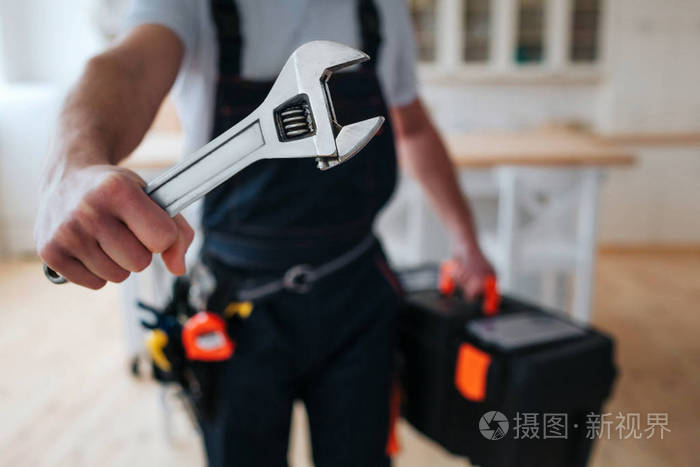 切去拿着工具箱的杂工视图, 手在靠近相机的手上扳手.他站在厨房里.
