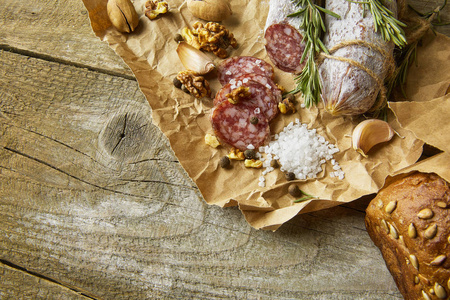 意大利腊肠, 含海盐, 迷迭香, 大蒜和坚果在纸上。质朴的风格。顶部视图
