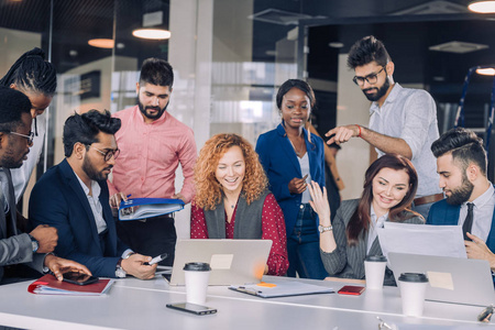 年轻的多民族工作小组交流围绕笔记本电脑聚集的想法照片