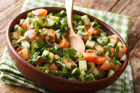 沙拉的黄瓜，西红柿，洋葱和草药特写在一个碗在桌子上。水平