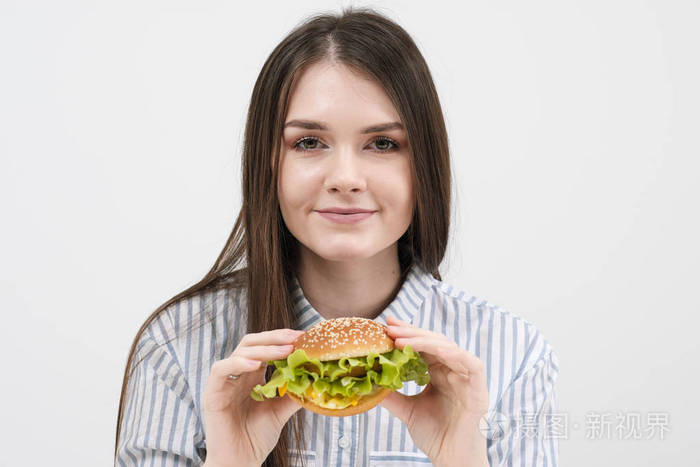 苗条的黑发女孩手里拿着一个汉堡包。在白色背景下, 饮食和适当营养的主题