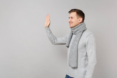 侧面看穿灰色毛衣围巾的年轻人挥手和问候，注意到有人孤立在灰色的墙壁背景上。 健康时尚生活方式真诚情感寒冷季节观念