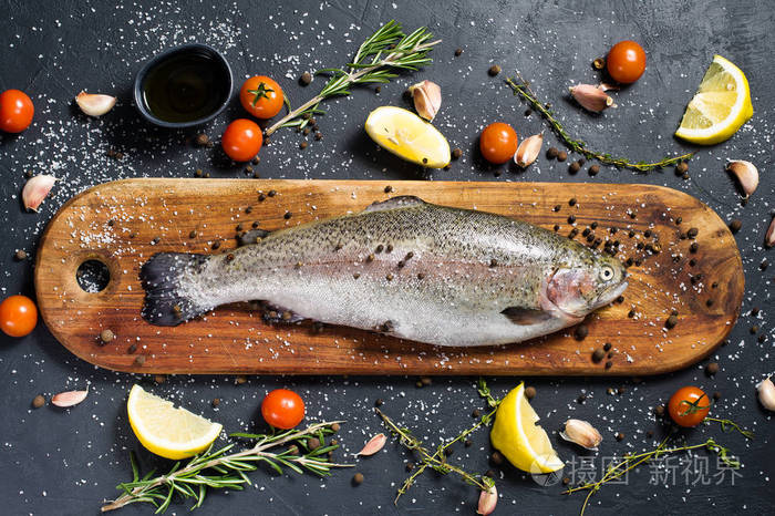 生鳟鱼在木制砧板上原料迷迭香柠檬西红柿大蒜盐胡椒黑色背景顶部视图