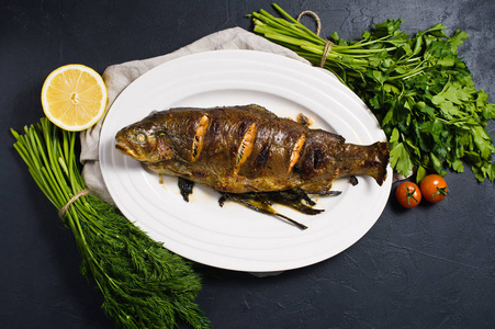 烤鳟鱼在一个白色的盘子里的迪尔和欧芹。 黑色背景顶部视图