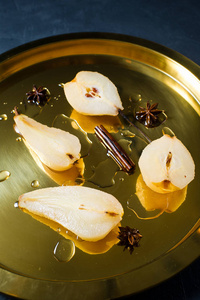 切成薄片的梨浸在白葡萄酒上煮熟的金托盘上。 黑色背景侧视图关闭