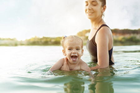 快乐的孩子。 妈妈第一次教她的小女儿游泳。 在炎热的夏天，女人抱着一个孩子在水里。 积极情绪和完全幸福