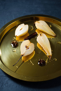 切成薄片的梨浸在白葡萄酒上煮熟的金托盘上。 黑色背景顶部视图