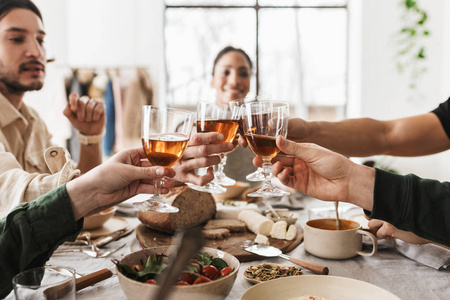 紧握着国际朋友手中的酒杯。 年轻的同事们在舒适的咖啡馆里愉快地庆祝着一起共进午餐