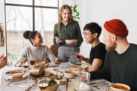 一群酷酷的国际朋友坐在满是食物的桌子旁,在舒适的咖啡馆里一起吃