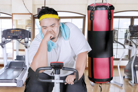 在健身中心用运动自行车锻炼后,精疲力竭的胖子看上去汗流浃背照片