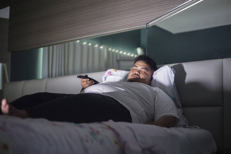 一位年轻的胖子在床上睡觉时拿着一台远程电视的照片照片