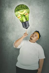 一个体贴的胖子穿着运动装用蔬菜指着灯泡照片